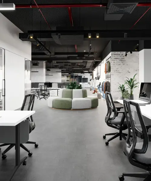 A modern office space featuring open workstations with black swivel chairs and white desks. In the center, there is a round, modular green and white seating arrangement. The office has a high ceiling with exposed ducts, plants, and a bright, minimalist design.